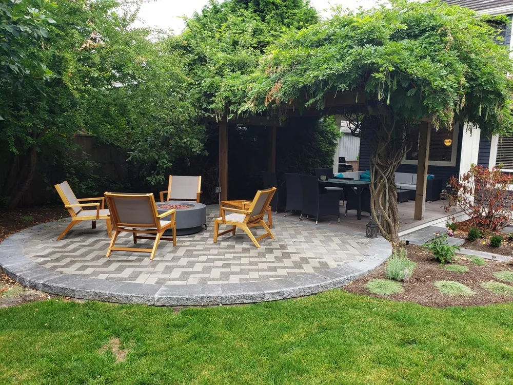 Circular herringbone paver patio with a fire pit and wooden chairs under a wisteria-covered pergola