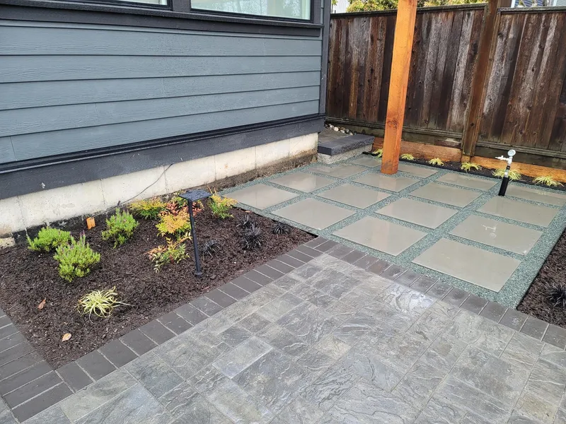 Backyard paver patio with landscape lighting fixtures beside new planting