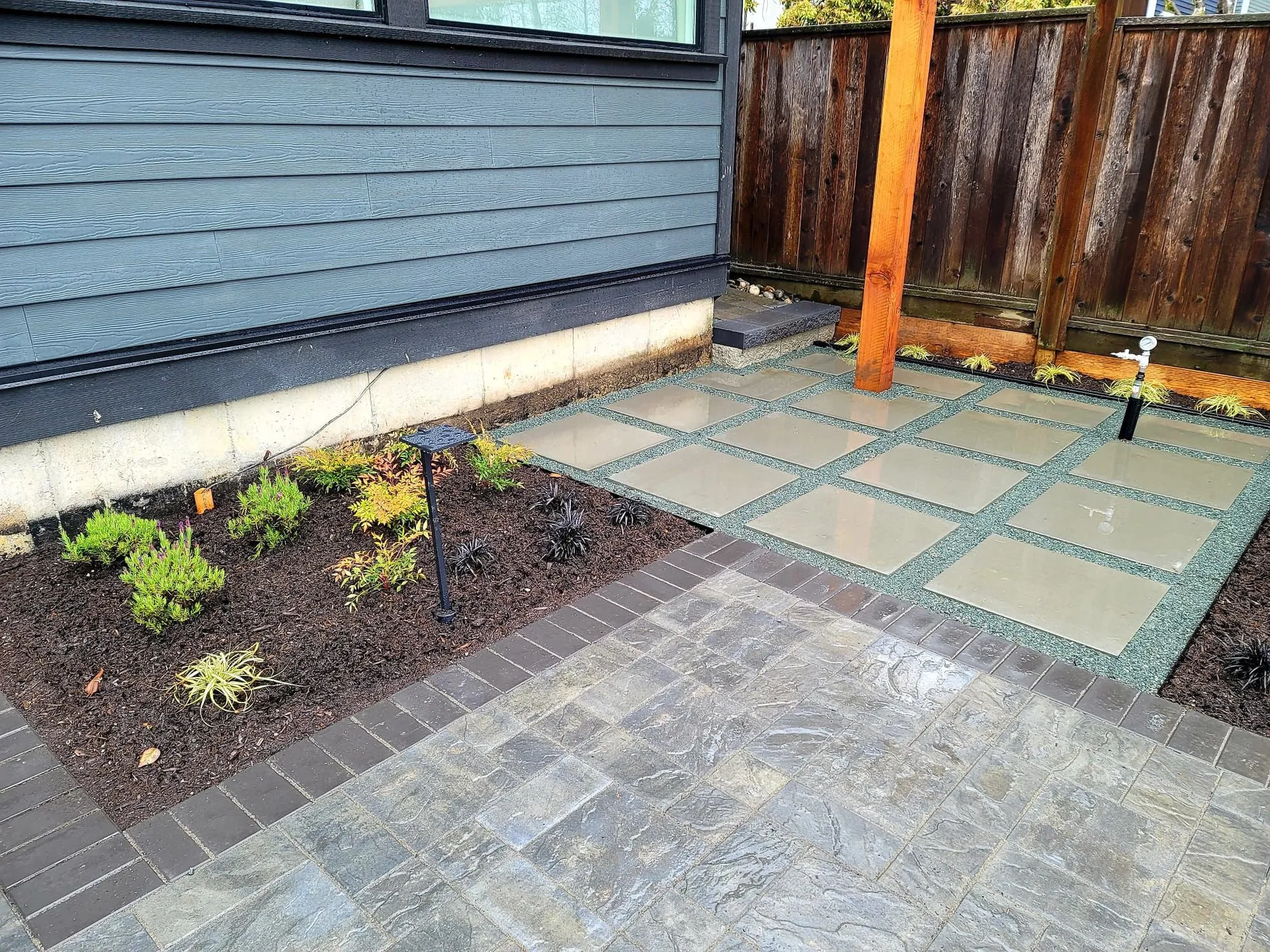 Planted garden bed with drip irrigation beside a paver patio