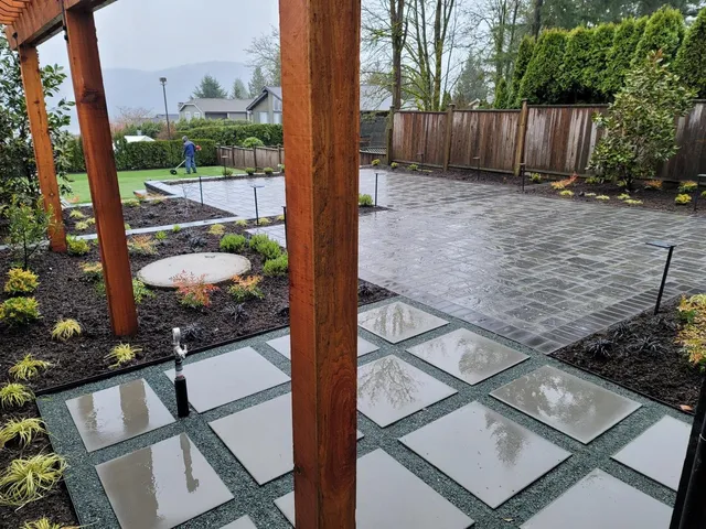 Wide view of the backyard: stepping-stone pavers under a cedar pergola, a paver patio, new beds with path lights and the lawn beyond