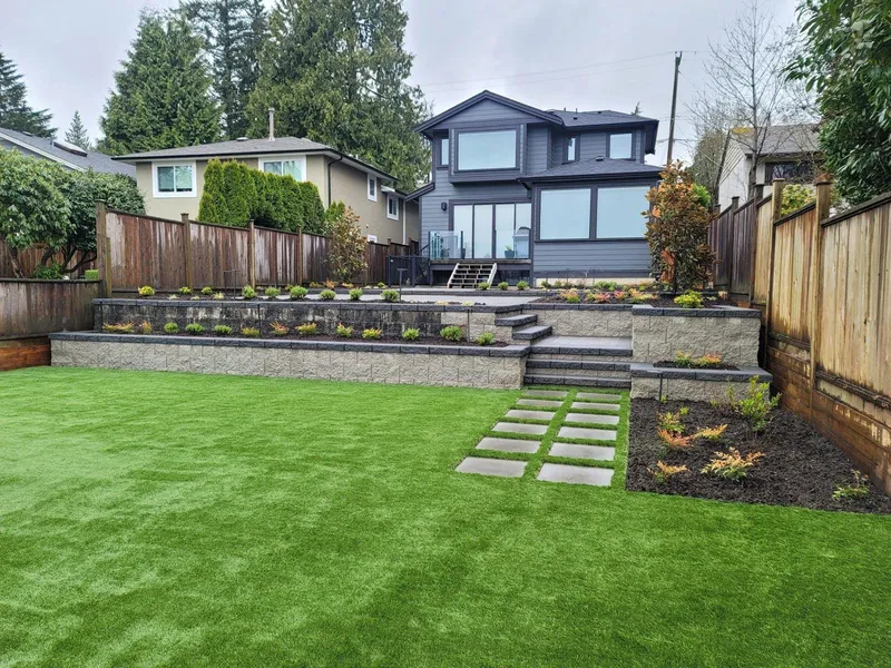 Finished backyard with artificial turf, a block retaining wall, steps and new planting