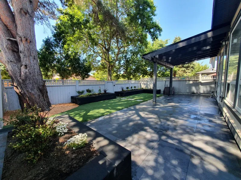 Porcelain tile patio under a covered structure with artificial turf and black planter boxes
