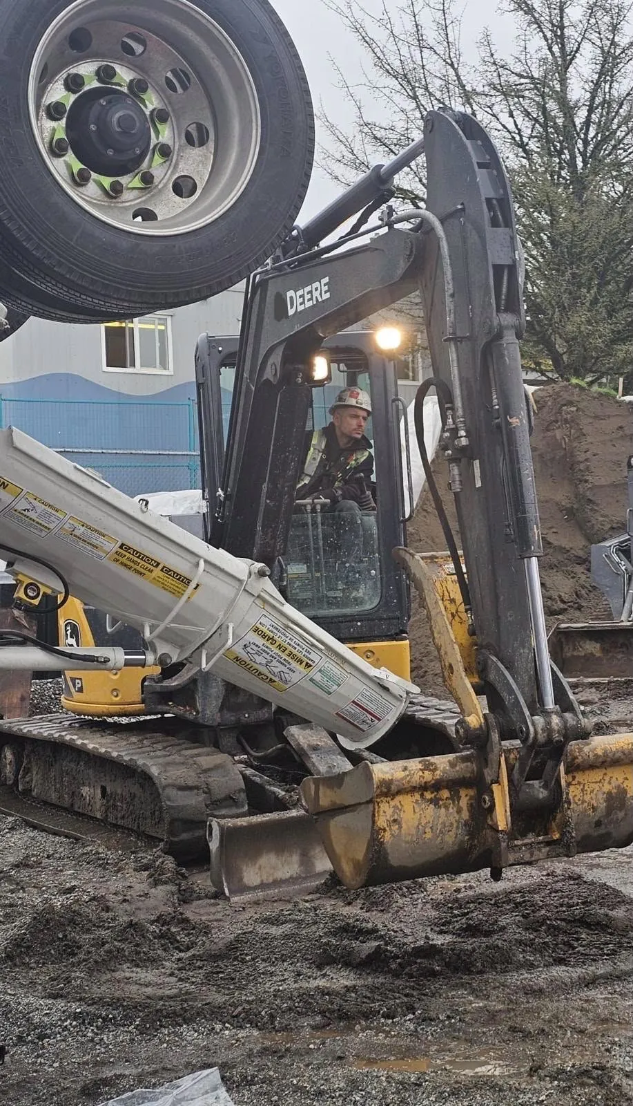 Operator in a mini excavator digging a trench beside a stockpile of soil