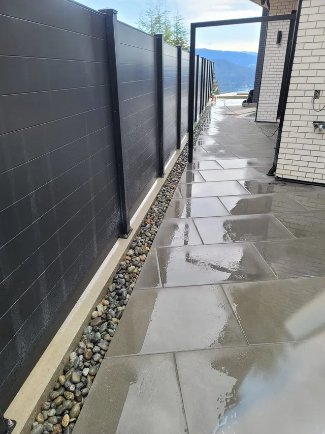 Large concrete pavers and river rock along a black privacy fence