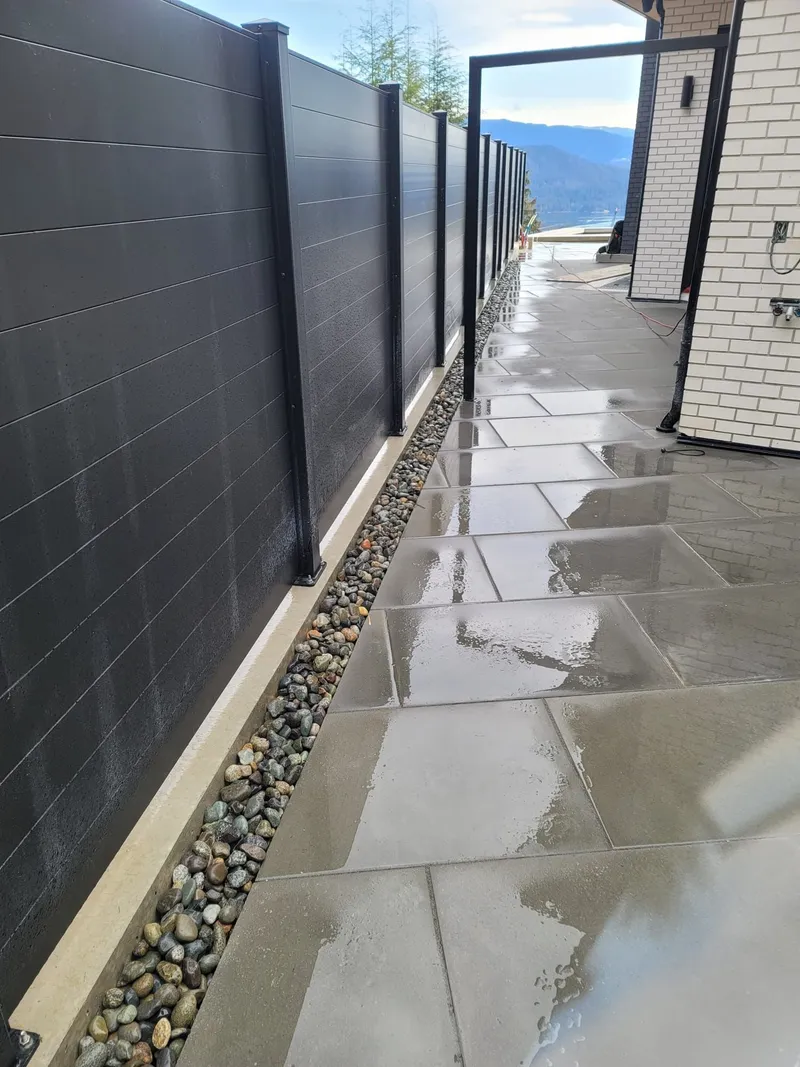Large concrete pavers and river rock along a black privacy fence