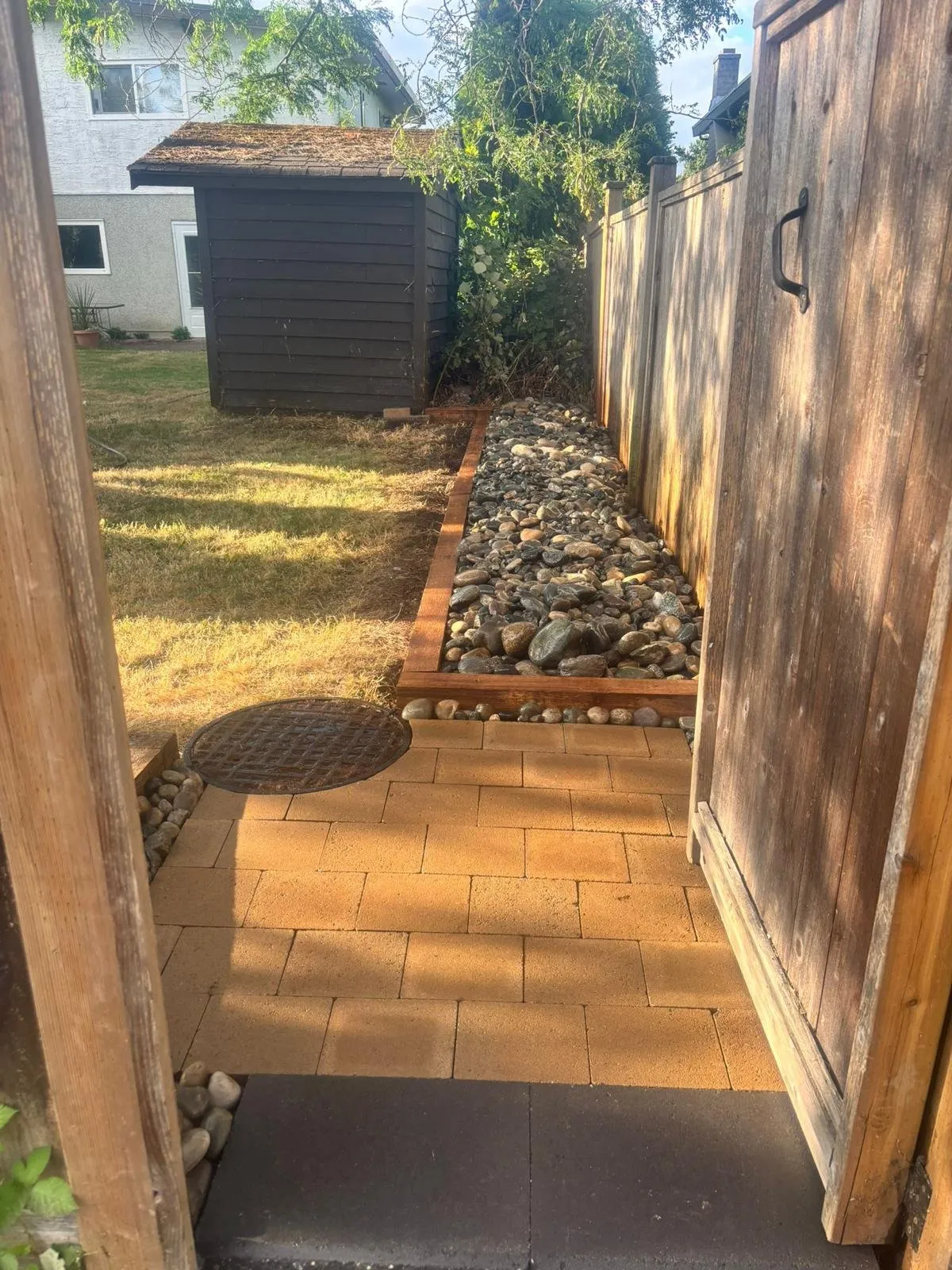 Side yard after: paver path with river rock drainage edge, seen through the new gate