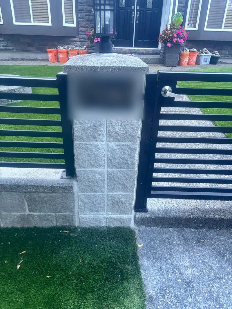 Black horizontal slat fence and gate with a stone pillar and artificial turf