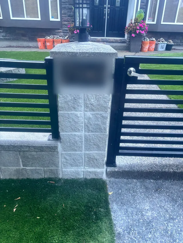 Stone pillar and black slat gate with artificial turf on both sides
